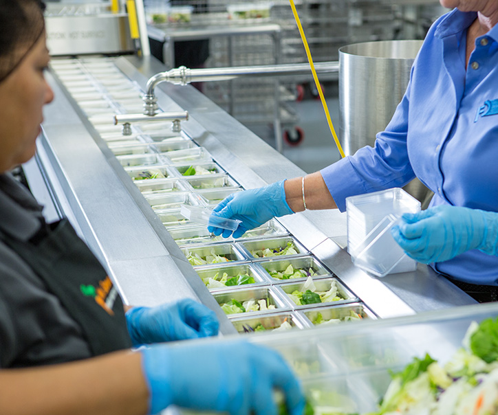 Tray sealing machine being loaded by food processing workers